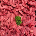 Raw sliced red meat arranged closely together, with a small green parsley garnish in the center, photographed from above.