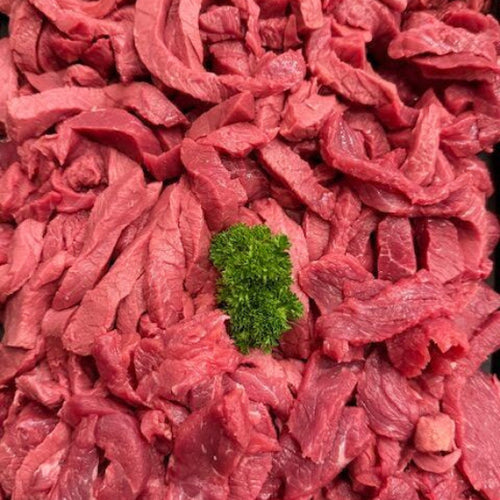 Raw sliced red meat arranged closely together, with a small green parsley garnish in the center, photographed from above.