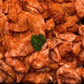 Raw marinated chicken pieces piled in a dark tray, coated with a reddish-orange seasoning mixture and garnished with a small green parsley sprig in the center.