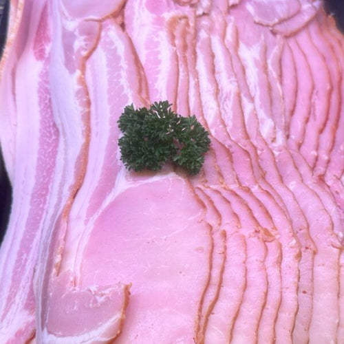 Slices of pink cured bacon stacked in a black tray, with a small green parsley garnish in the center.