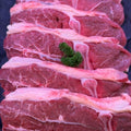 Several thick raw beef steaks with visible marbling and fat layers arranged vertically on a dark surface, with small green herb garnish placed on top.