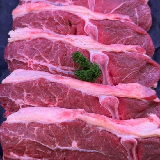Several thick raw beef steaks with visible marbling and fat layers arranged vertically on a dark surface, with small green herb garnish placed on top.