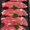 Five raw beef chuck steaks arranged vertically on a dark tray, each garnished with a small sprig of green parsley.