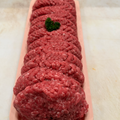 Raw ground meat patties arranged in a pink rectangular tray, with a small green garnish on top, photographed on a light countertop.