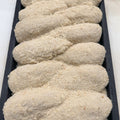 Six breaded CHICKEN KIEVS coated in a thick beige breadcrumb mixture and arranged in a black rectangular baking tray.