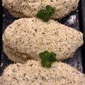 Three breaded chicken breast fillets topped with a green parsley garnish, arranged in a row on a dark baking tray.