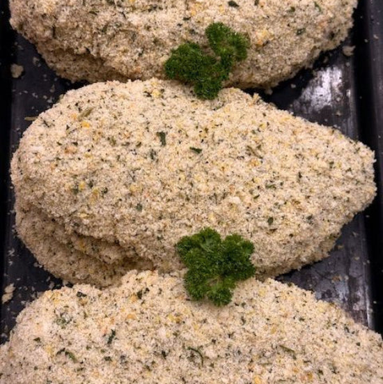 Three breaded chicken breast fillets topped with a green parsley garnish, arranged in a row on a dark baking tray.