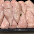 Raw breast fillets of chicken arranged in a black plastic tray on a white surface.