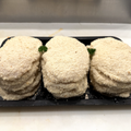 Three stacks of round, breaded chicken schnitzel, arranged on a black tray with small green garnish pieces on a white countertop.