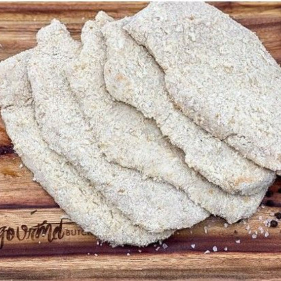 Four thick, rectangular, breaded chicken schnitzels stacked on a wooden cutting board with seasoning, rosemary, and a garlic clove. Available at Robina Quality Meats