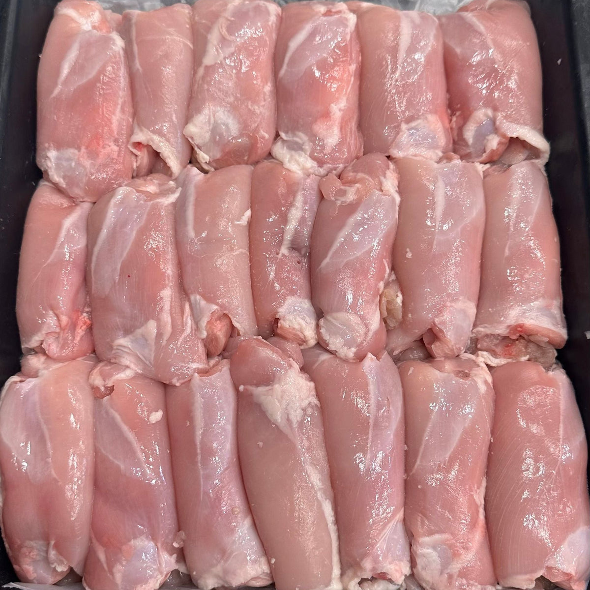 Raw chicken thigh fillets arranged in rows inside a black tray or container.