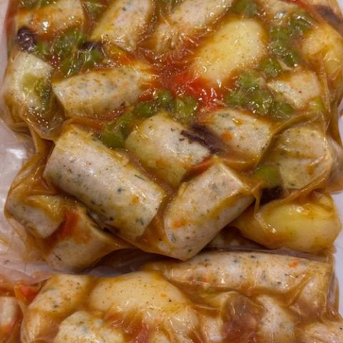 Close-up of curry sausages, green peppers, red tomatoes, and a light sauce, photographed on a white surface.