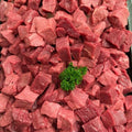 Chunks of raw red beef or lamb meat piled together, with a small green parsley garnish in the center, photographed from above.