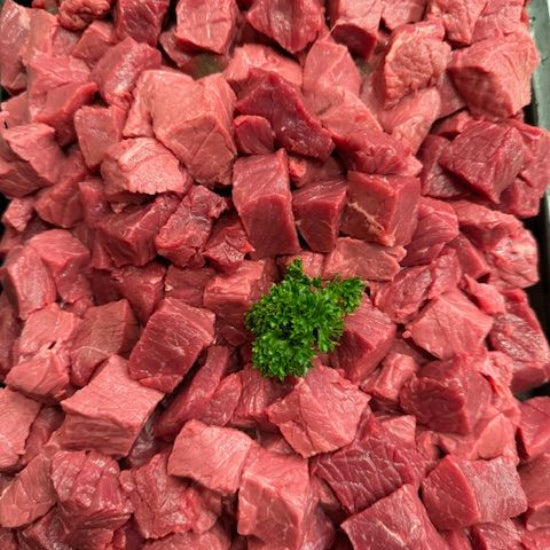 Chunks of raw red beef or lamb meat piled together, with a small green parsley garnish in the center, photographed from above.