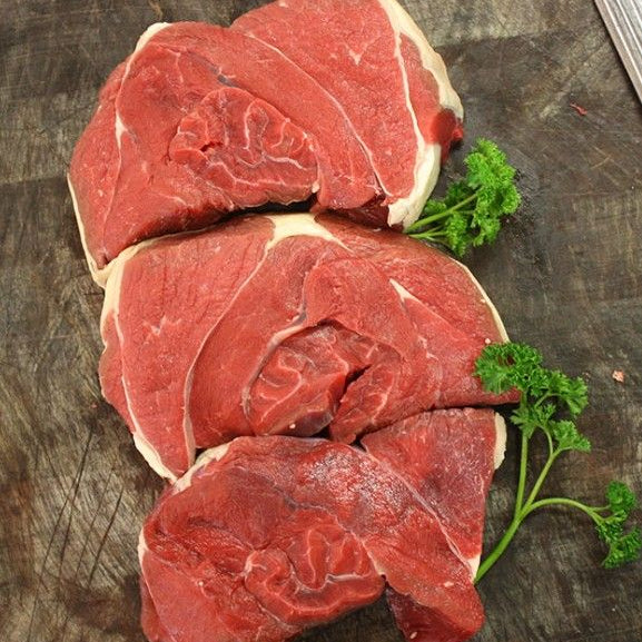 Three raw beef tenderloin slices with visible fat marbling, arranged on a dark wooden cutting board with parsley garnish.