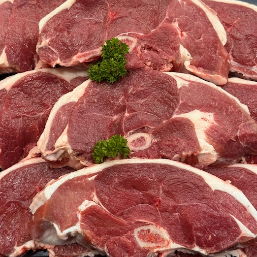 Raw lamb chops stacked on a dark surface, with small green parsley garnish placed on top.