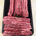 Raw lamb ribs arranged on a black tray, with vertical long strips on top and stacked horizontal strips below, photographed from above on a light beige surface.