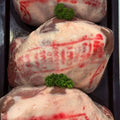 Three raw lamb roasts in a black tray, each topped with a small green parsley garnish. The meat has red stamped markings and is photographed from above.