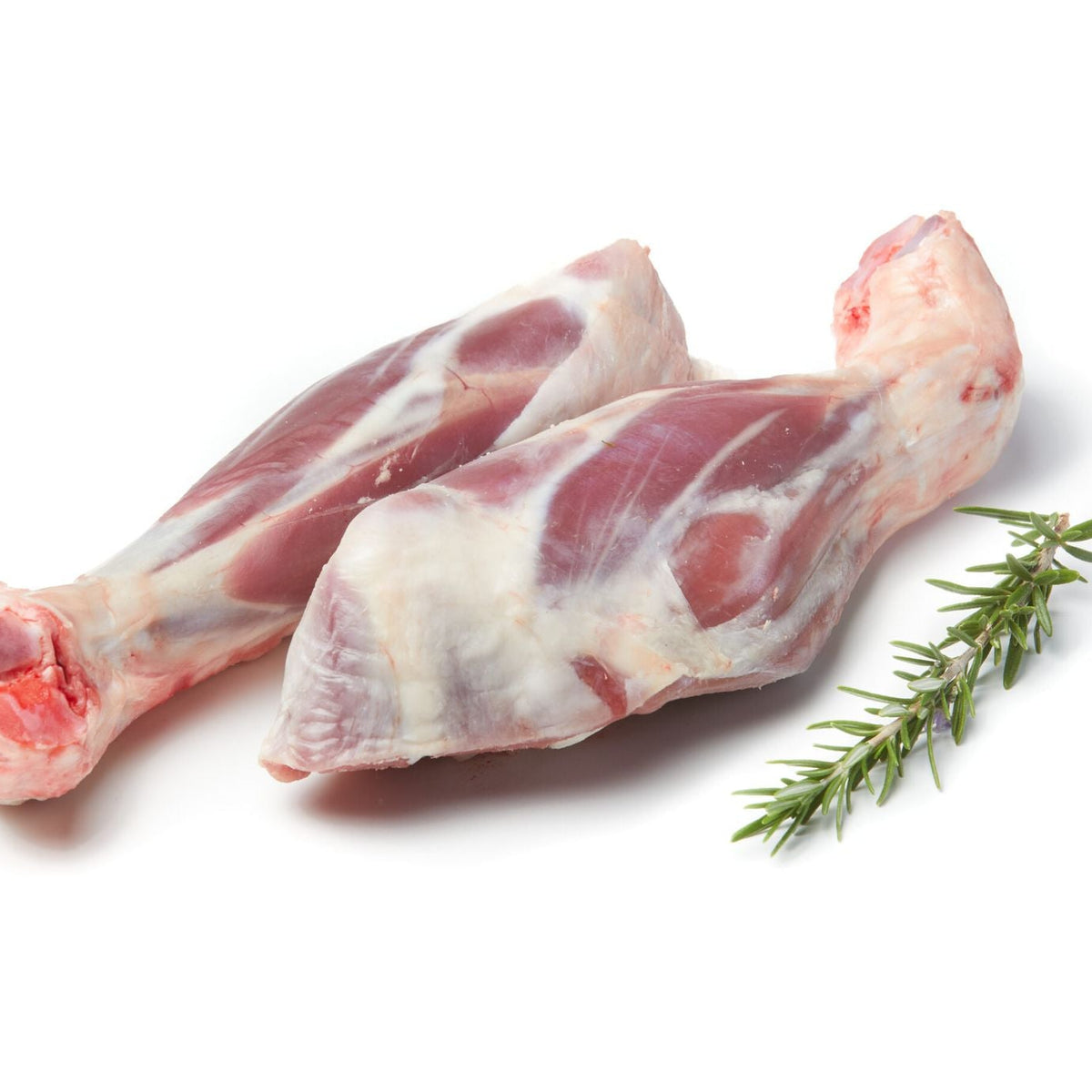 Two raw lamb shanks with visible bone ends, arranged on a white background with a small green herb sprig beside them.