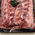 Raw pork baby back ribs visible fat marbling, sealed in a clear plastic tray with a small green parsley garnish on top, photographed from above on a light surface.