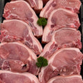 Raw pork chops arranged in a black tray with small green parsley garnishes between pieces.