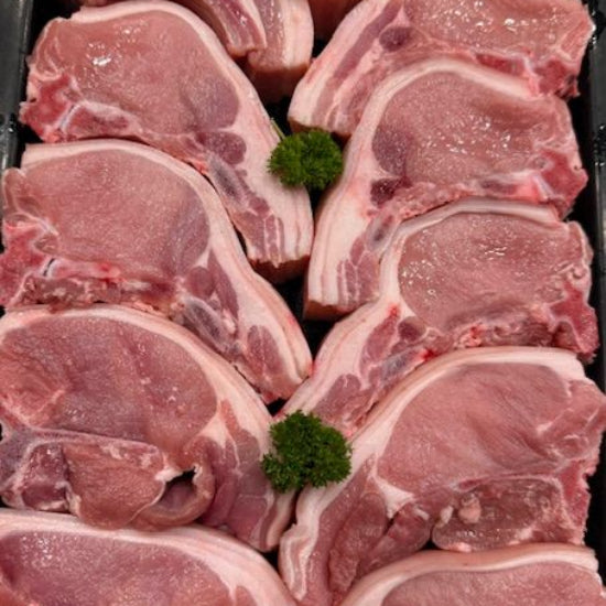 Raw pork chops arranged in a black tray with small green parsley garnishes between pieces.