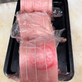 Three rolled pieces of pork loin roast, wrapped in clear plastic and tied with string, arranged on a black tray on a light beige countertop. Available to Robina Quality Meats