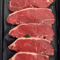 Six raw beef tenderloin steaks arranged vertically in a black plastic tray, garnished with small green parsley sprigs.