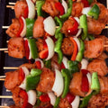 Raw chicken skewers with red bell peppers, green bell peppers, and white onions on a black tray.