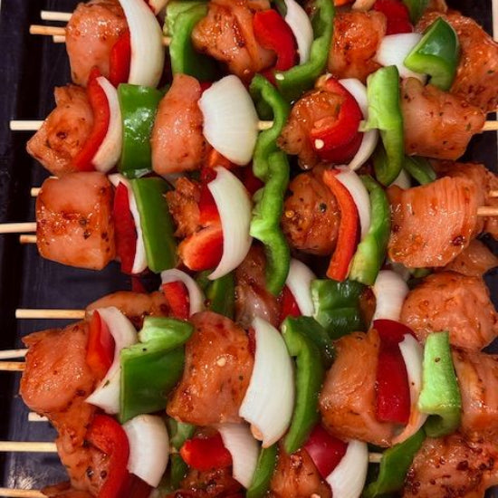 Raw chicken skewers with red bell peppers, green bell peppers, and white onions on a black tray.