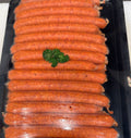 A black plastic tray filled with multiple thin beef sausages, wrapped in clear plastic and topped with a small green herb garnish, photographed on a light countertop.