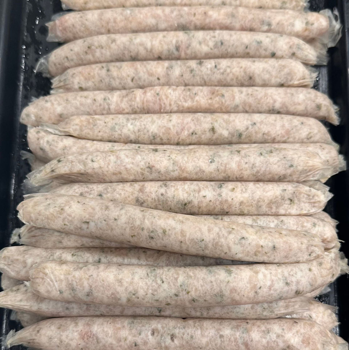 Multiple raw sausage links arranged in rows inside a black plastic tray.