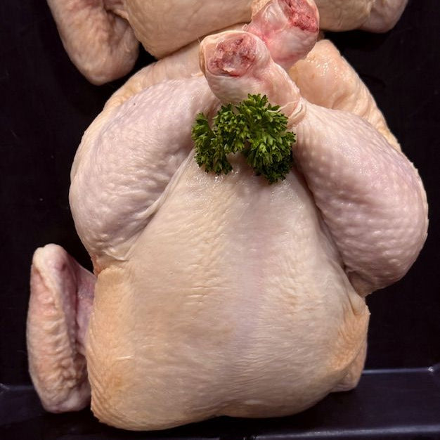 A whole raw chicken photographed from above on a black surface, with a small green parsley garnish placed on its chest.