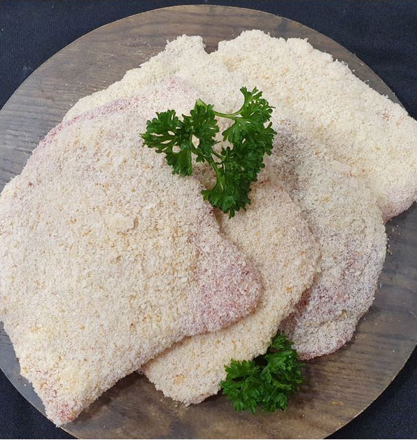 Four breaded cutlets topped with fresh green parsley, arranged on a round wooden serving board against a dark background.